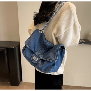 Detail of blue denim tote bag with silver chain strap worn by a model in sweater