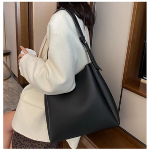 Stylish large black faux leather tote bag shown on a model in a cozy indoor setting