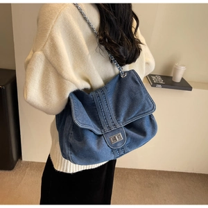 Close-up of denim shoulder bag featuring silver metal twist lock and chain strap detail