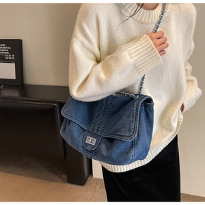 Detail of blue denim shoulder bag with silver chain strap and metal lock closure on model