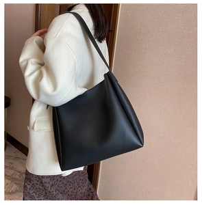 Detailed side view of a large black faux leather tote bag worn by a model in casual attire