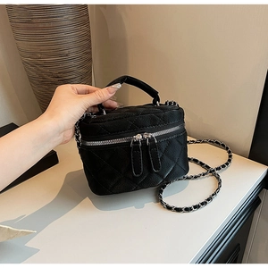 Detail of black quilted mini bag with gold chain strap and dual zippers in hand
