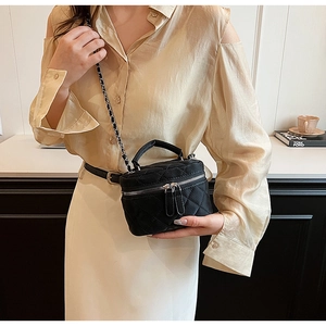 Close-up of black quilted mini chain bag worn as a crossbody with gold hardware