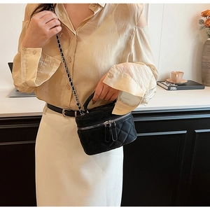 Detail of a black quilted leather mini bag with gold chain strap on a modern tabletop