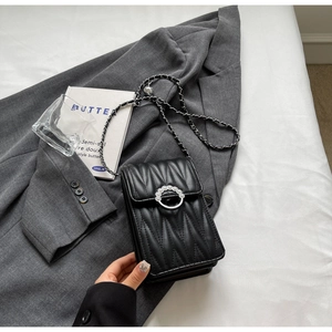 Dettaglio borsa trapuntata nera con fibbia a perla su sfondo di un blazer grigio