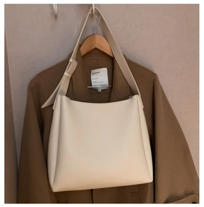 Detail of soft cream leather tote bag hanging on a wooden hanger with a brown wool coat
