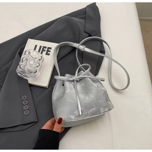 Détail du sac seau argenté avec revêtement métallique et nœud coulissant sur tissu gris