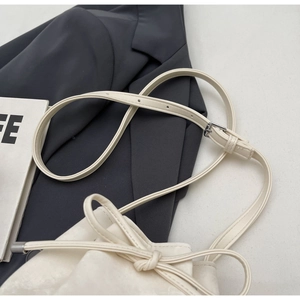 Détail d'un sac seau blanc crème avec bandoulière réglable et nœud déco sur un blazer gris