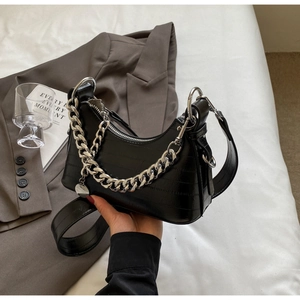 Detail of black faux crocodile leather crescent bag with silver chain on grey blazer