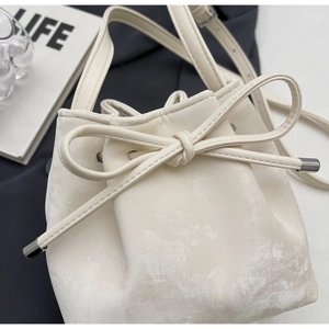 Détail d'un sac seau blanc avec nœud coulissant et cuir texturé sur un fond moderne