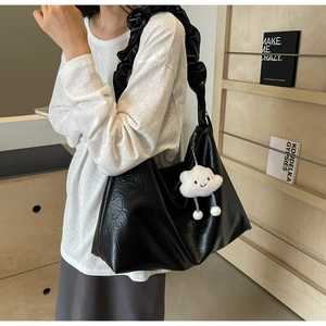 Detail of black leather hobo bag with ruffled shoulder strap and cloud pendant charm