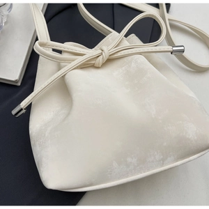 Gros plan du sac seau à cordon crème avec texture cuir et embouts métalliques argentés