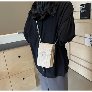 Dettaglio della borsa trapuntata crema con fibbia di perle indossata da modella in interni