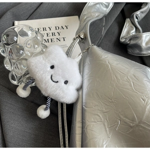 Detail of a white plush cloud charm with smiley face on a silver metallic tote bag