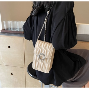 Dettaglio della borsa a tracolla beige trapuntata con fibbia a perla e catena su modella