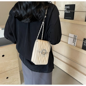 Dettaglio della borsa trapuntata beige con chiusura di perle e tracolla in catena di pelle