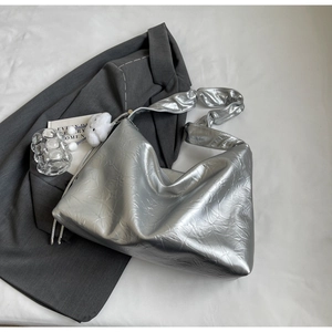 Close-up of metallic silver tote bag with pleated texture on a grey blazer