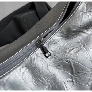 Detail of silver metallic tote bag featuring pleated texture and silver metal zipper