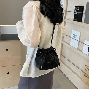 Sac seau noir brillant minimaliste avec nœud élégant porté par un mannequin en intérieur