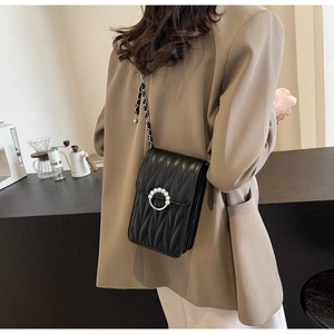 Modella che indossa una borsa trapuntata nera con catena e fibbia di perle in un caffè