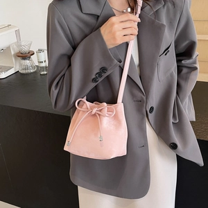 Sac seau rose chic à cordon avec nœud décoratif et fine bandoulière porté par un mannequin