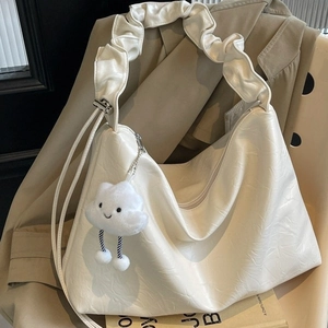 Minimalist beige tote bag with textured cloud handle and plush charm in soft indoor lighting