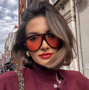 Close-up of tortoise shell oversized sunglasses with gold T-logo and orange lenses