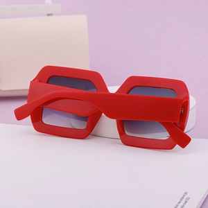 Détail de lunettes de soleil carrées rouges avec verres dégradés sur un plateau blanc