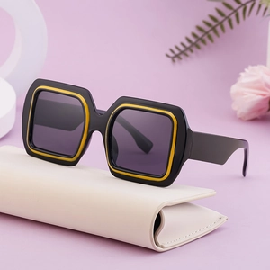 Lunettes de soleil carrées noires avec touches jaunes et étui en cuir crème sur fleurs