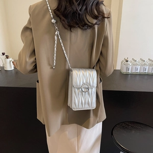 Borsa a tracolla argento con catena e fibbia di perle indossata da modella in un caffè