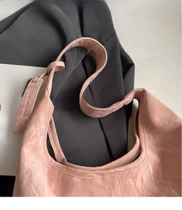 Detail of pink pleated faux leather tote bag with smooth shoulder strap on grey blazer