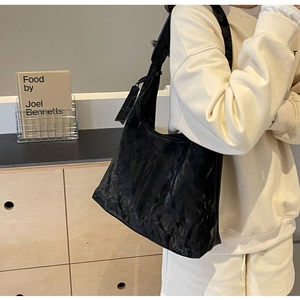 Detail of black glossy pleated hobo bag showing texture and drape on a model's shoulder