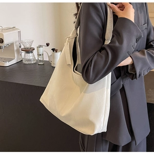 Detail of a large white minimalist leather shoulder bag worn with a professional suit