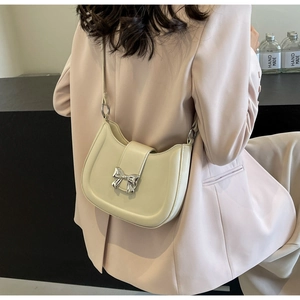 Detail der cremefarbenen Halbmond-Tasche mit silberner Schleifenschnalle und rosa Blazer