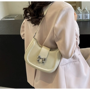 Detail einer cremeweißen Schultertasche mit silberner Schleifenschnalle am Model