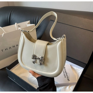 Detail einer cremeweißen Halbmond-Schultertasche mit einer silbernen Schleifenschnalle