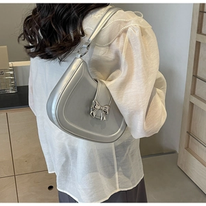 Detail der silbernen Halbmond-Schultertasche mit Metallschleife und elegantem Kettenstil