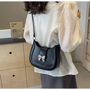 Schwarze Leder-Satteltasche mit Silberschleife am Model in gemütlichem Innenraum