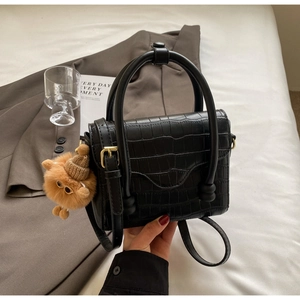 Detail of black faux crocodile skin pattern handbag with a cute teddy bear charm