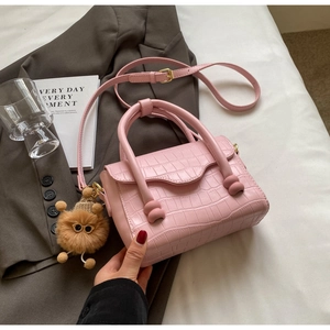 Detailed view of pink croc-embossed handbag featuring a brown pom-pom charm and strap