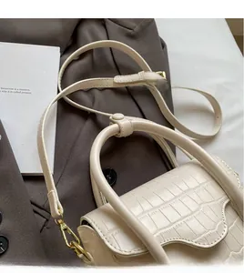 Detail of cream stone pattern crossbody bag with golden hardware on a dark blazer