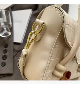 Detail of glossy gold metal hook and beige crocodile embossed leather handbag