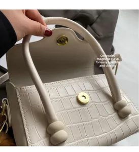 Close-up of white crocodile pattern handbag featuring a magnetic snap closure and gold hardware