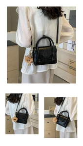 Detail of black faux leather handbag with crocodile pattern and plush animal charm