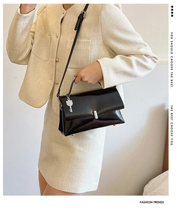 Macro view of black leather crossbody bag with silver buckle and model's beige suit