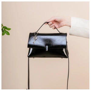 Detail of black glossy handbag with silver metal buckle and key-shaped charm detail