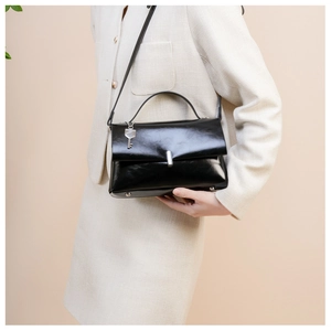 Elegant black oil leather crossbody bag detail with silver key pendant on white outfit