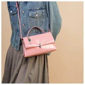 Detail view of pink glossy leather bag with silver lock and key charm on shoulder