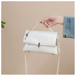 Close-up of white leather handbag featuring silver key charm and polished metal buckle