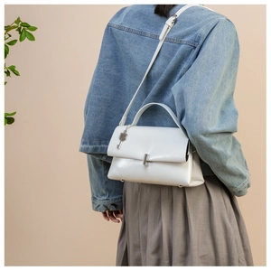 Detail view of white leather shoulder bag featuring silver clasp and metal key charm